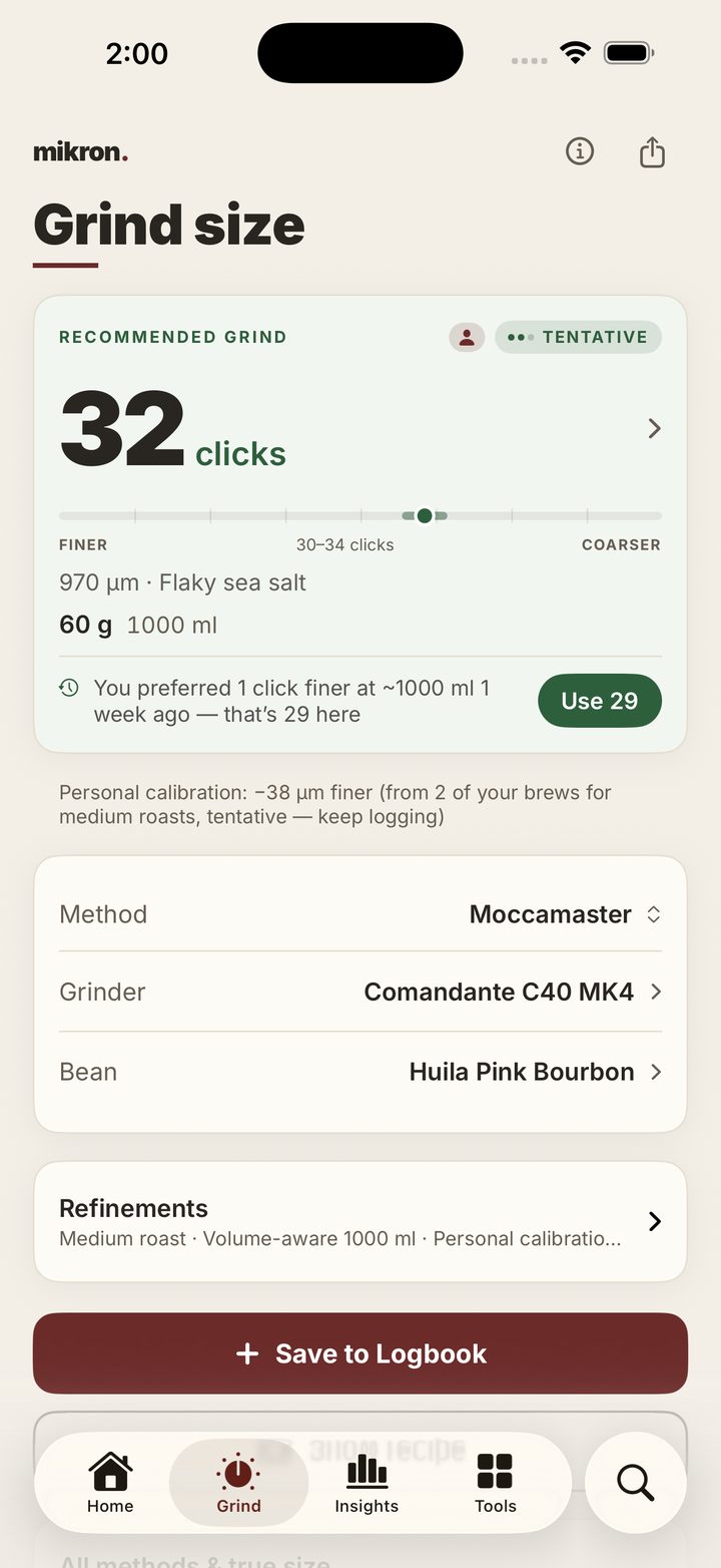 mikron. running on iPhone. The Grind screen recommends 32 clicks — 970 microns, a coarse grind like flaky sea salt — for a Moccamaster, a Comandante C40 MK4 and a bag of Huila Pink Bourbon, and marks that recommendation ‘tentative’. Below it the app recalls ‘you preferred 1 click finer at ~1000 ml 1 week ago — that’s 29 here’ beside a Use 29 button, and notes a personal calibration of 38 microns finer drawn from 2 of your brews for medium roasts.